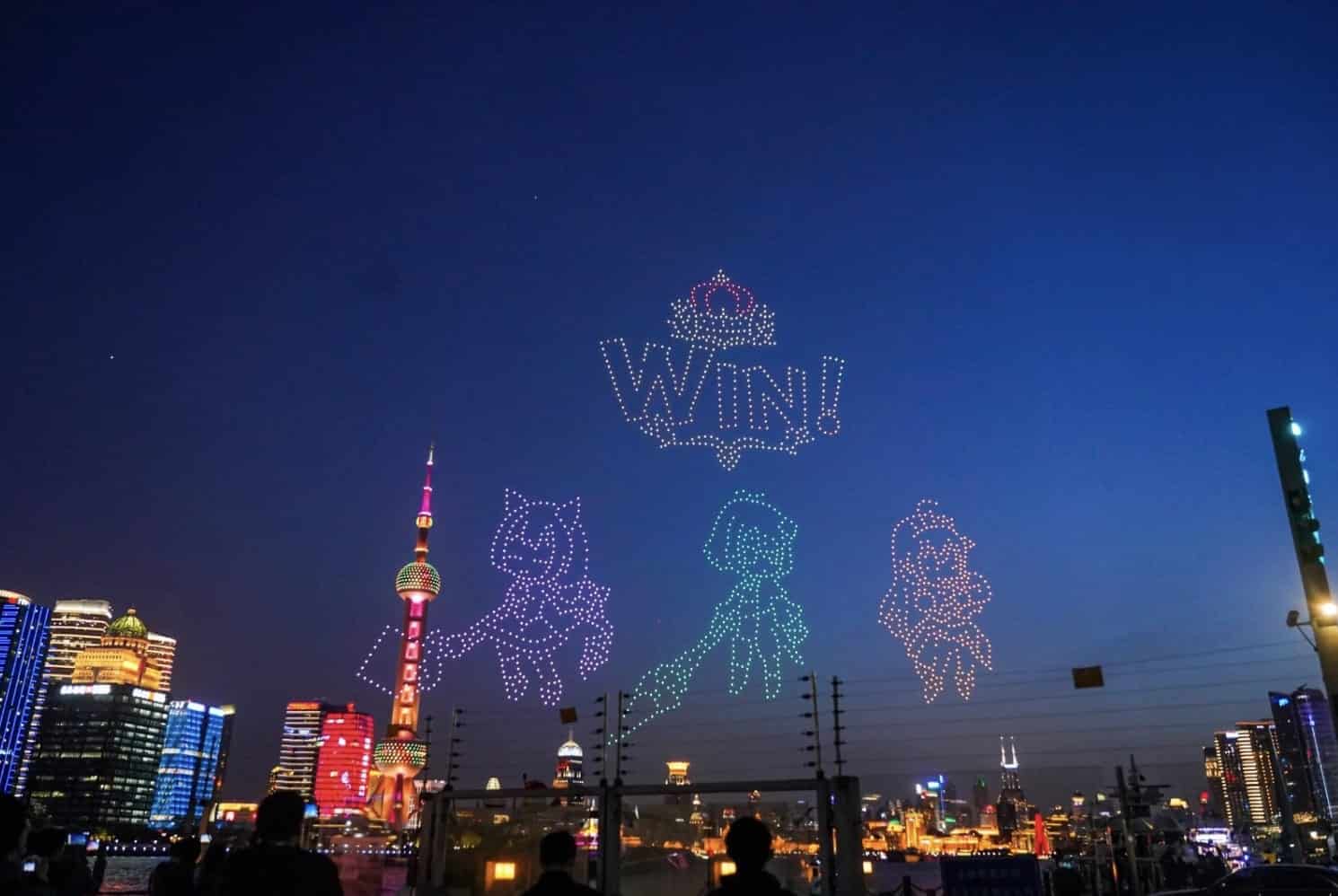 Drone light show spelling WIN with game characters above the Shanghai skyline at night.