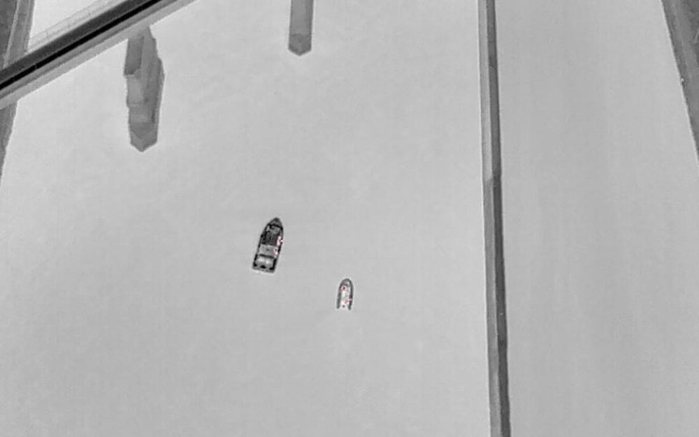 Thermal drone image of two boats on a river beside a bridge at night.