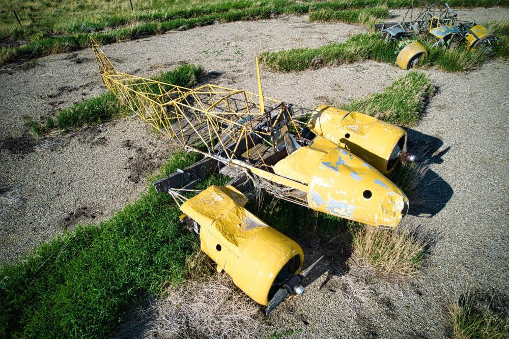 Salvaged Avro Anson airframe parts embedded in the gravel and grass of the installation.