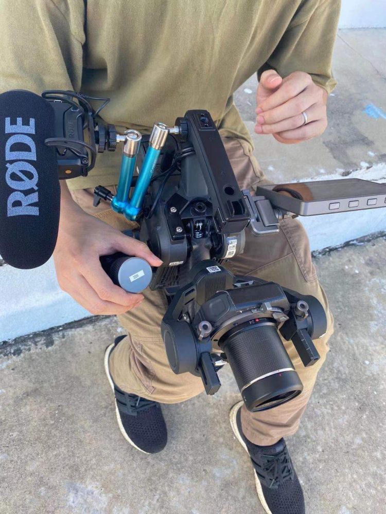 Operator kneeling with the DJI gimbal rig fitted with a Rode shotgun microphone.