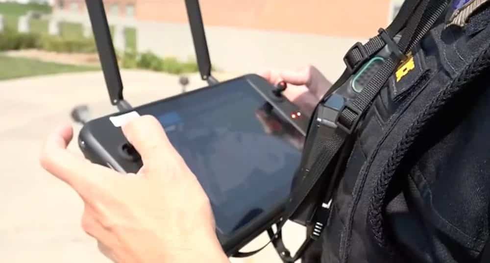 An officer works a drone controller with a tablet while wearing a tactical vest.