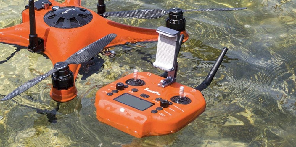 SplashDrone 4 and its orange waterproof controller floating in clear shallow water.