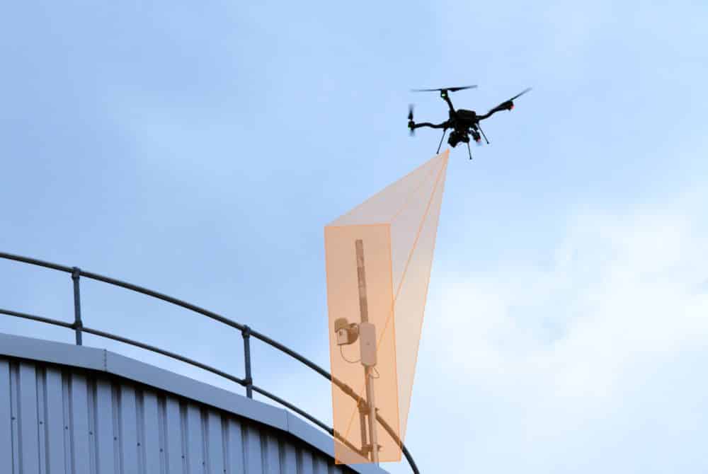 Inspection drone hovering beside a dish antenna mounted on infrastructure.