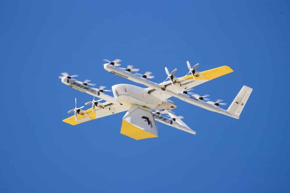 White and yellow Wing delivery drone banking against a solid blue backdrop.