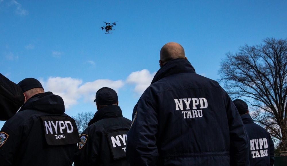 NYPD Technical Assistance Response Unit officers watching a drone fly in a blue sky.