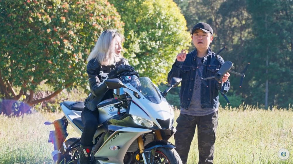 Two presenters outdoors with a motorcycle in a leaked drone review video.