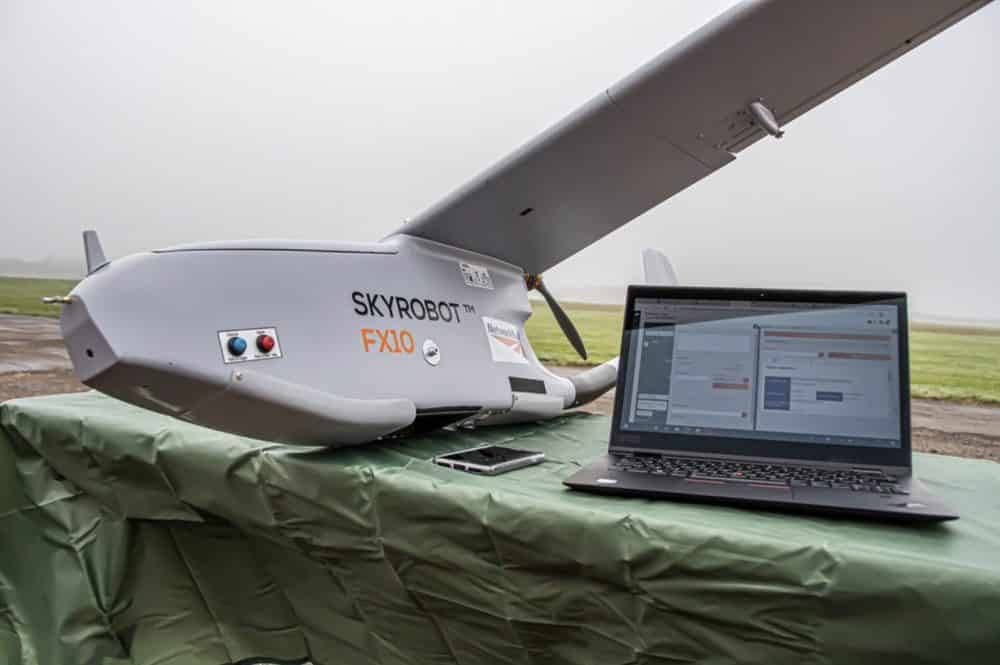 SkyRobot FX10 fixed-wing drone parked beside a laptop ground station outdoors.