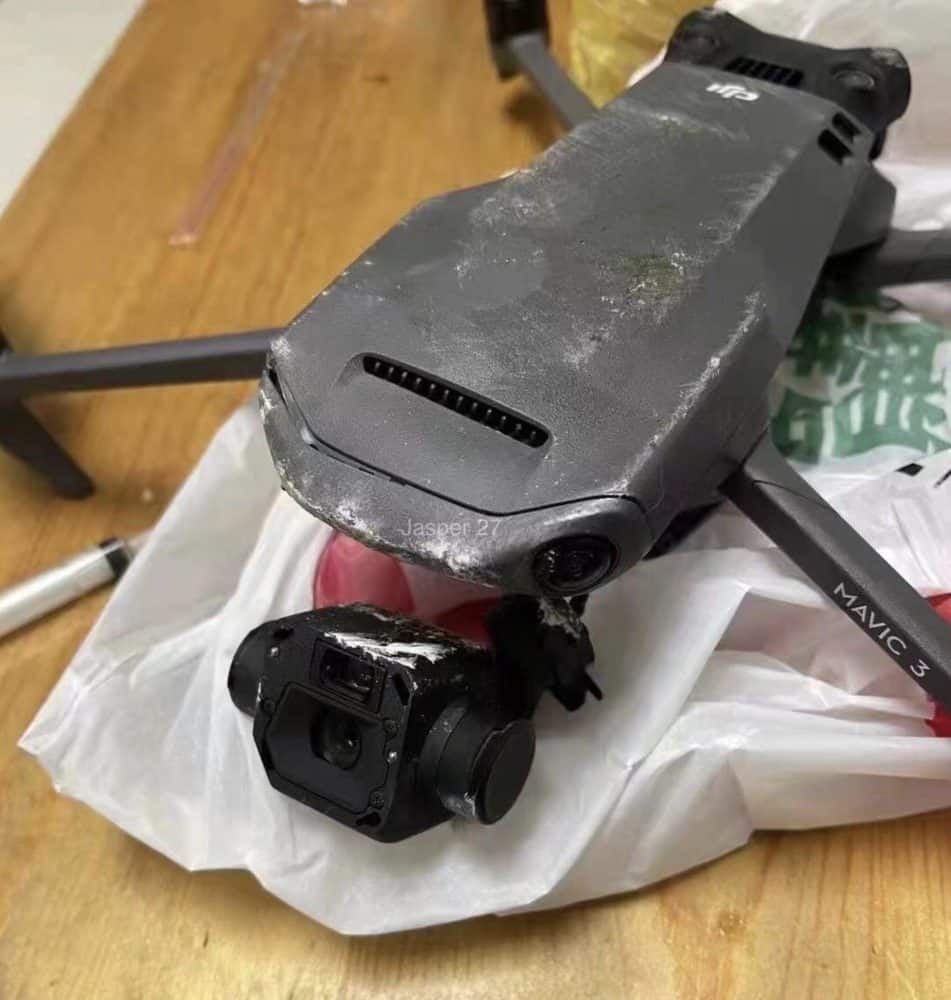 Crashed DJI Mavic 3 on a table with a scuffed shell and dangling gimbal camera.