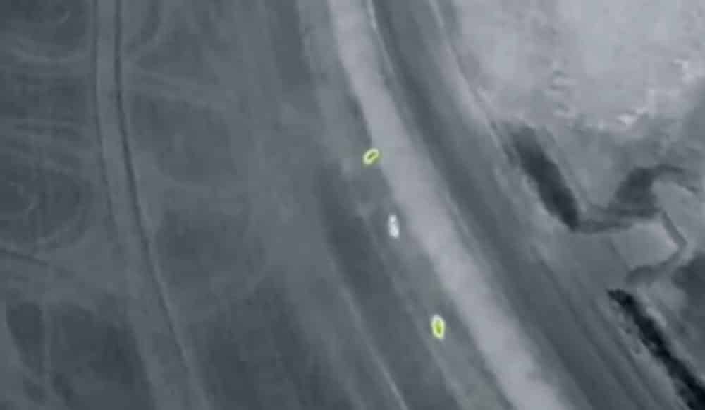 Thermal drone footage marking small heat signatures along a dark field edge.