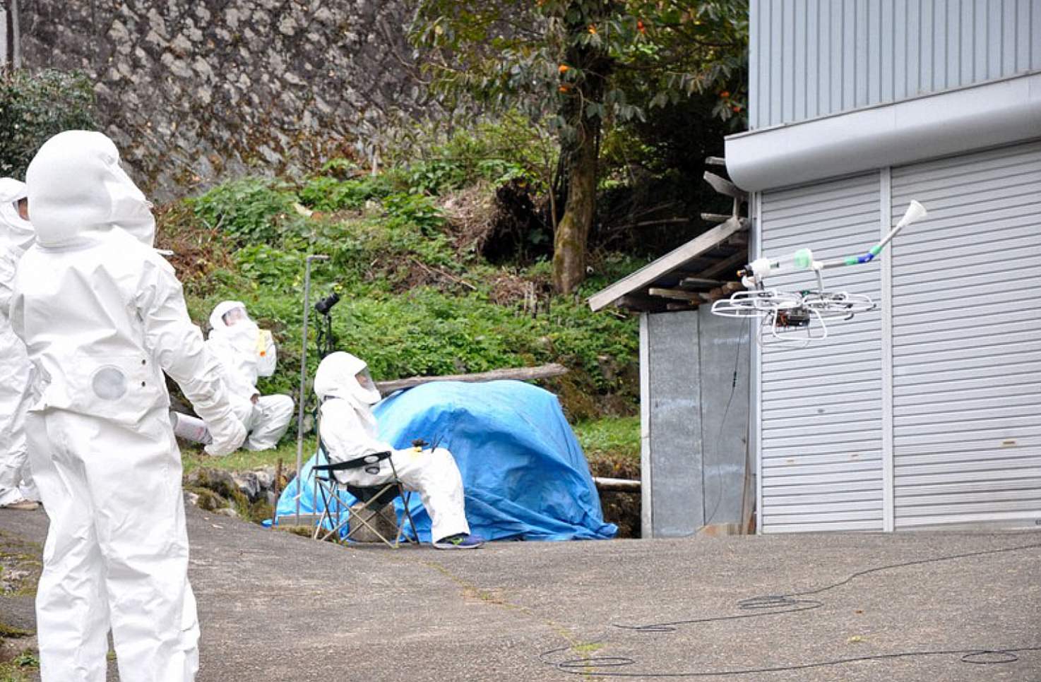 Pest control crew in white protective suits directing the vacuum drone outdoors.