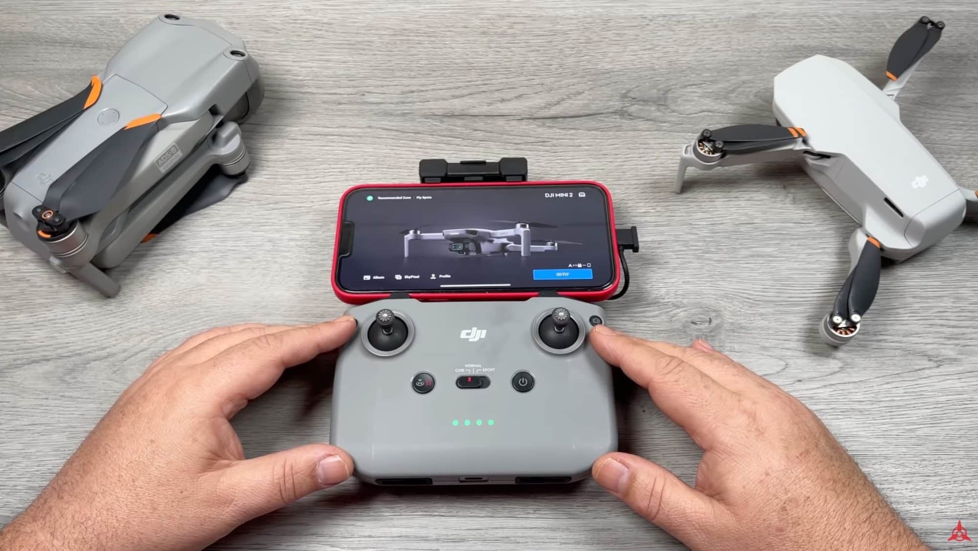 Hands working the DJI Fly app on a controller between two folded drones.