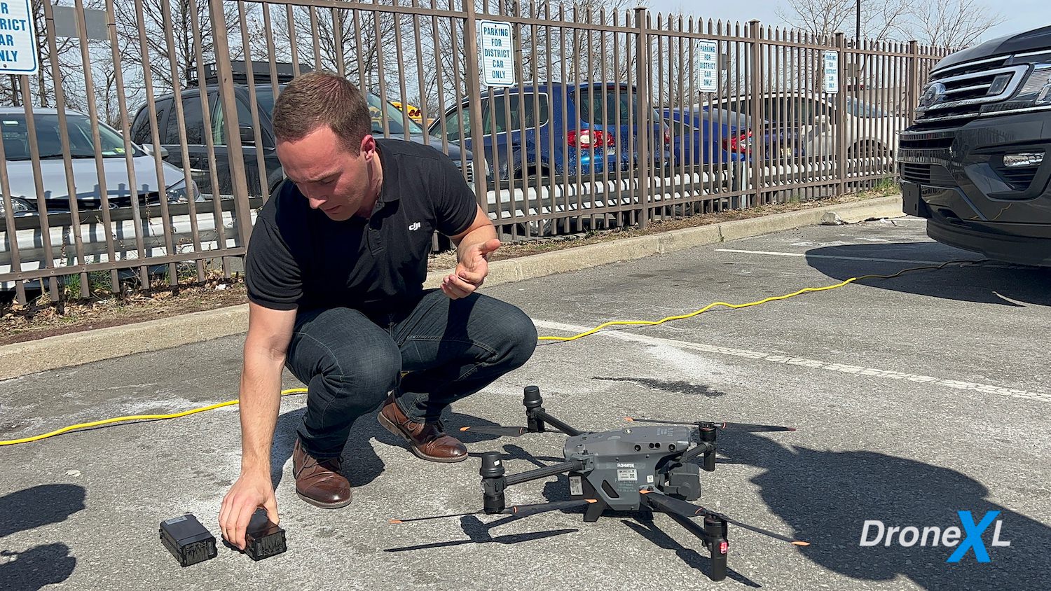 Presenter crouches beside a DJI Matrice 30 on pavement at a demo event.