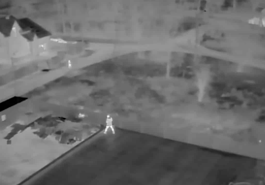 Night-vision aerial frame showing a lone figure standing on a road.