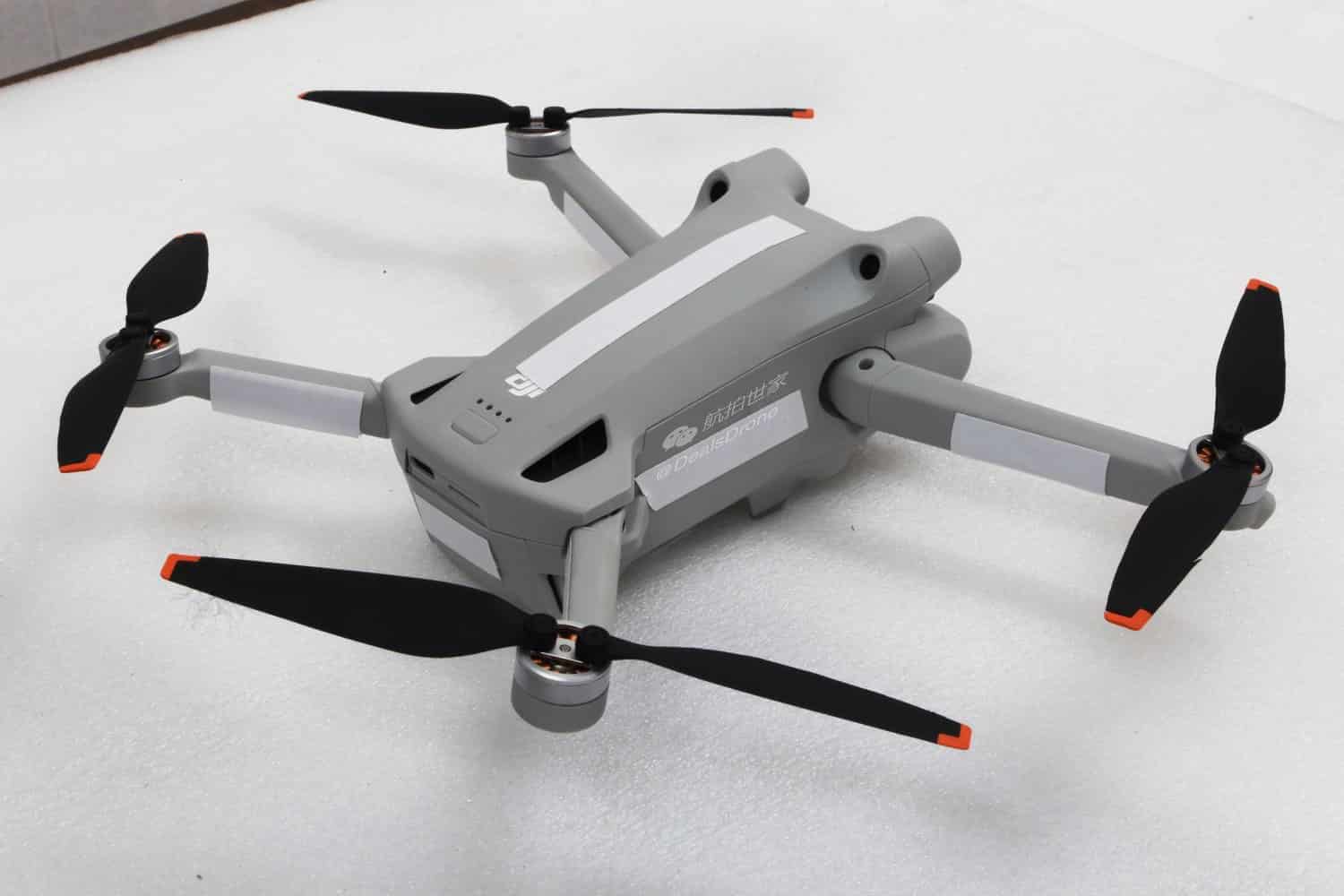DJI Mini 3 Pro sits unfolded on a white surface with propellers extended.
