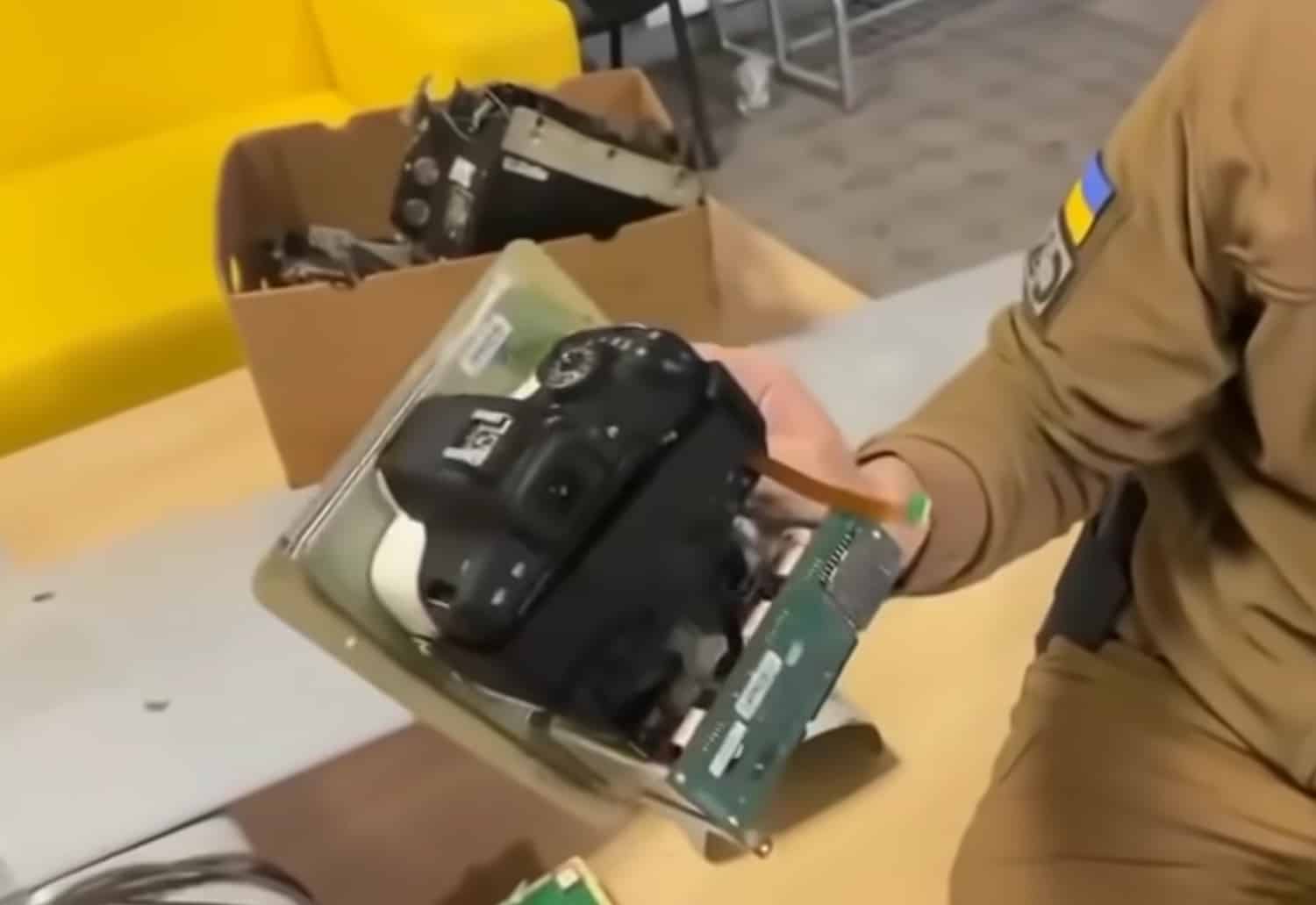 A soldier with a Ukrainian flag patch lifts the camera tray from a cardboard box.
