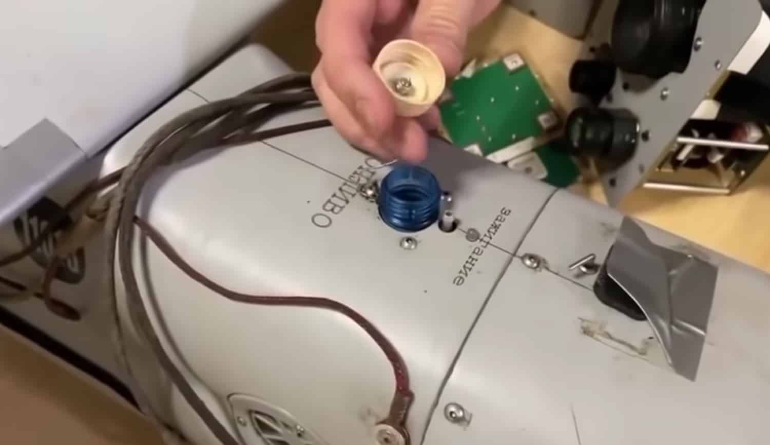 A hand holds a plastic bottle cap above the fuel filler on a drone fuselage.