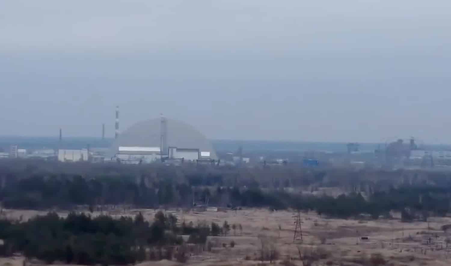 Distant aerial of the Chernobyl containment arch across the exclusion zone landscape.
