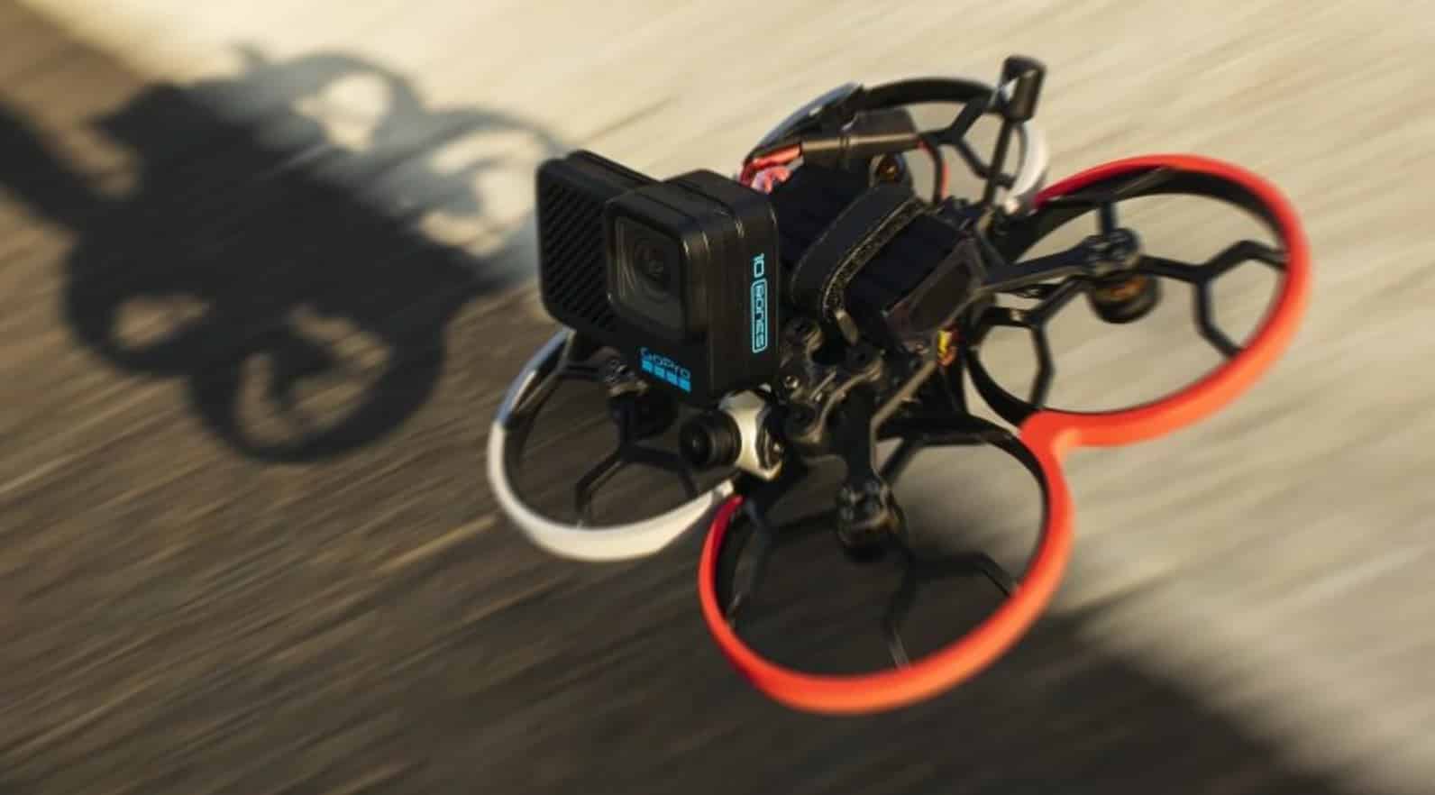 FPV cinewhoop with red ducts carrying a GoPro Bones camera in fast flight.