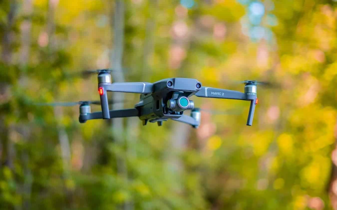 DJI Mavic 2 hovering in front of blurred yellow autumn foliage.