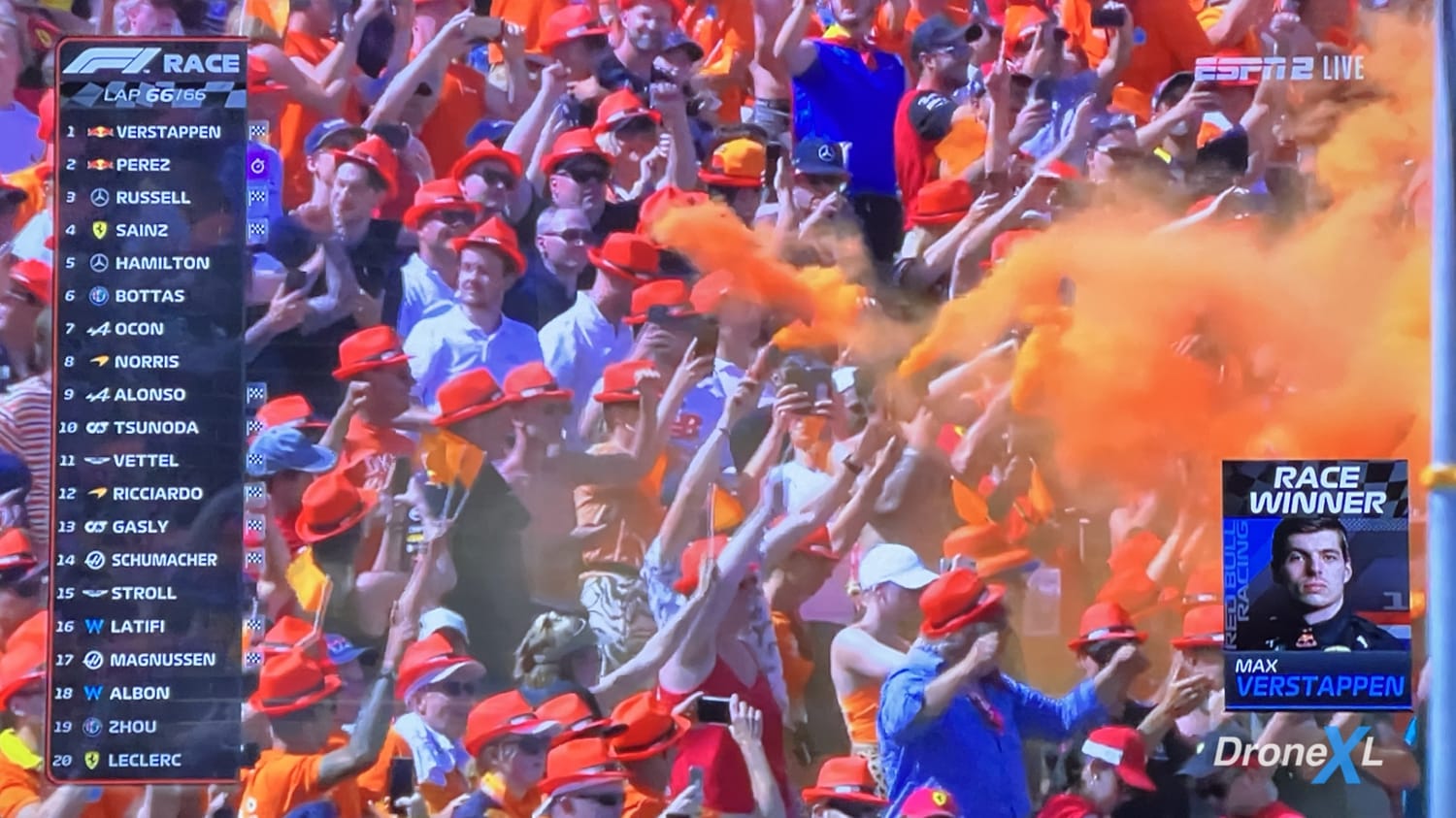 F1 broadcast frame of orange-clad fans with flares beside the Race Winner Verstappen graphic.