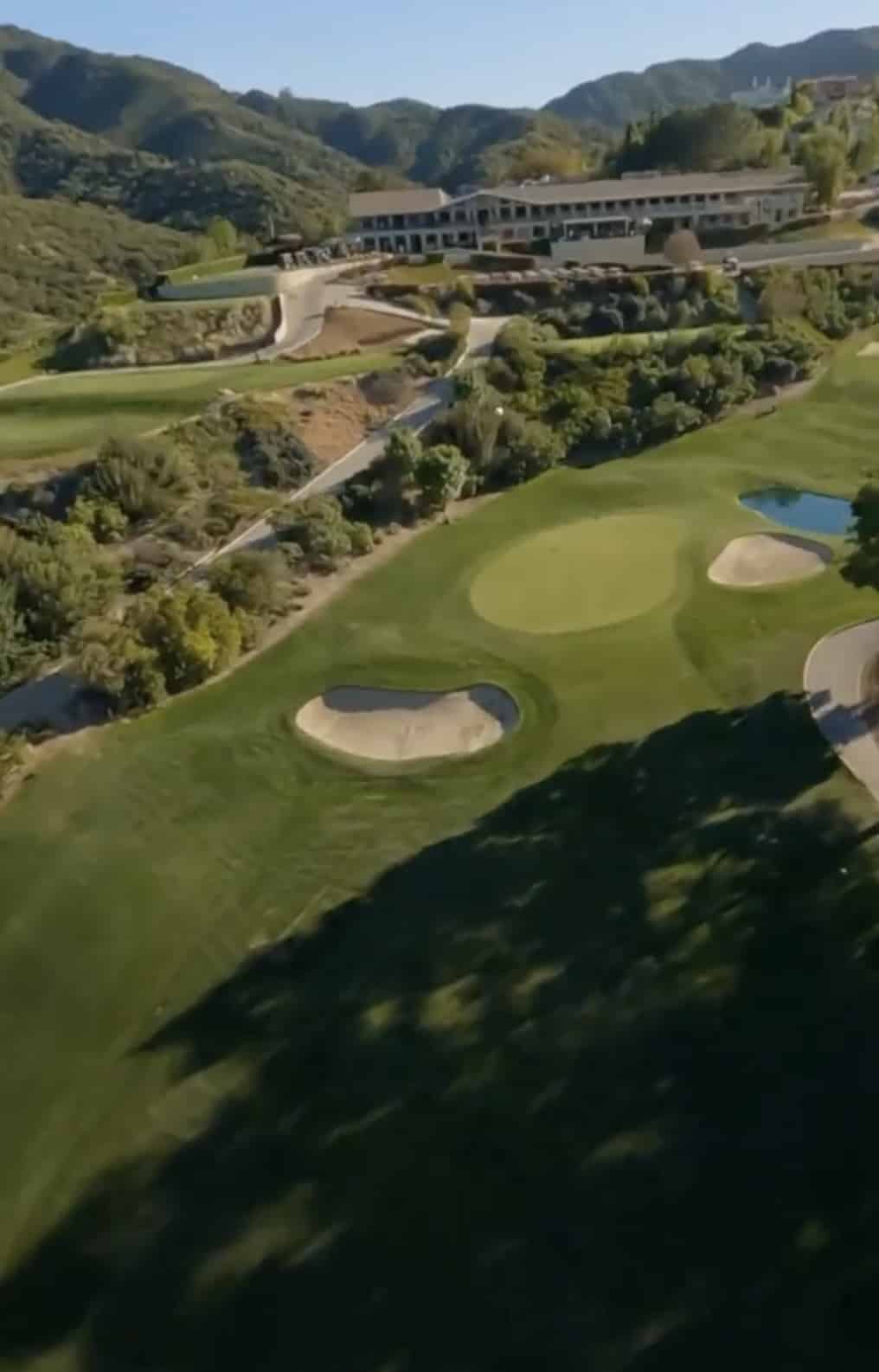 Aerial view of a hillside golf course with bunkers beside a resort building.