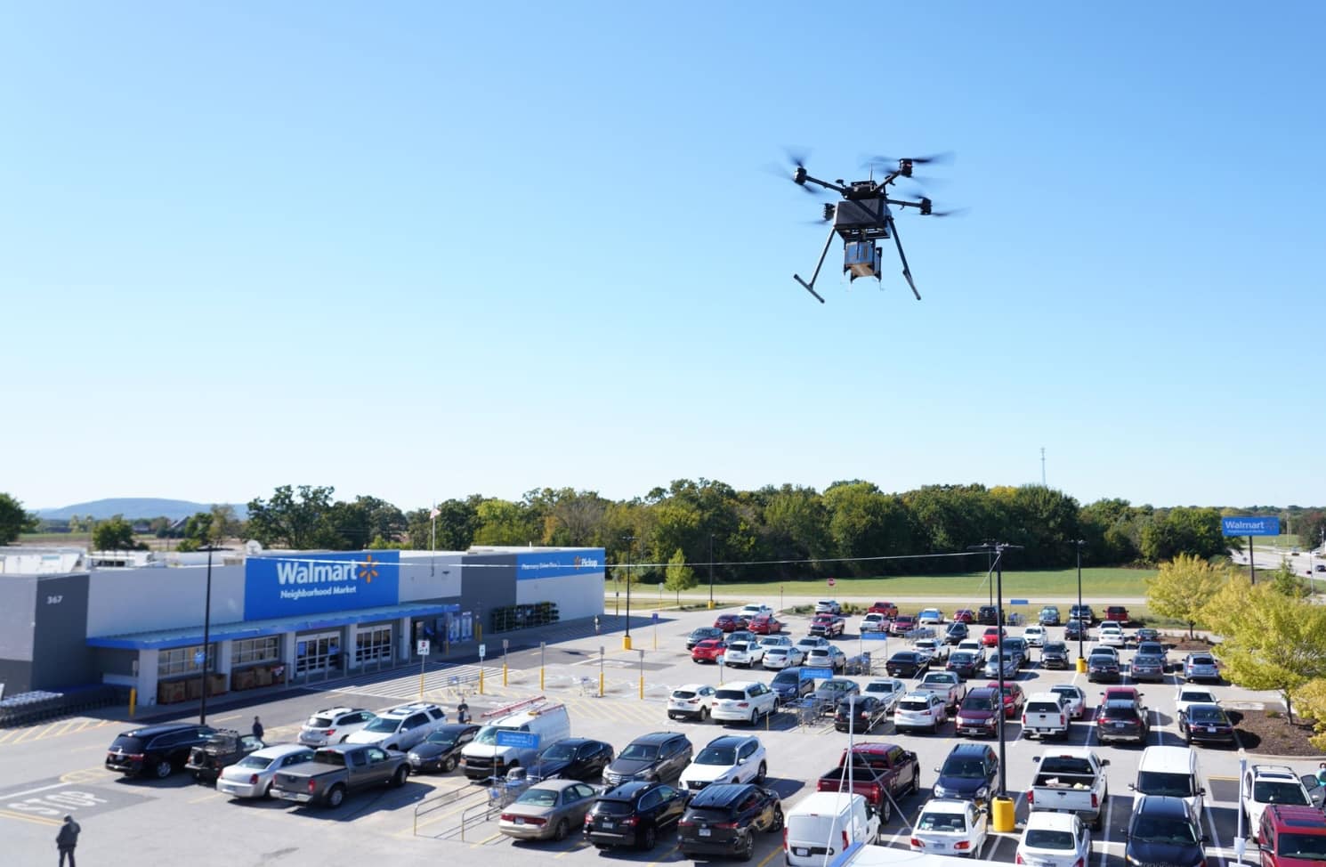 Delivery drone climbing above a Walmart store and its busy parking lot.