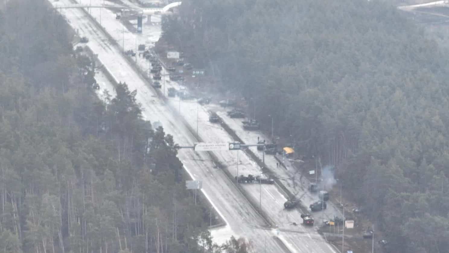Aerial view of a burning military convoy destroyed along a forest road.