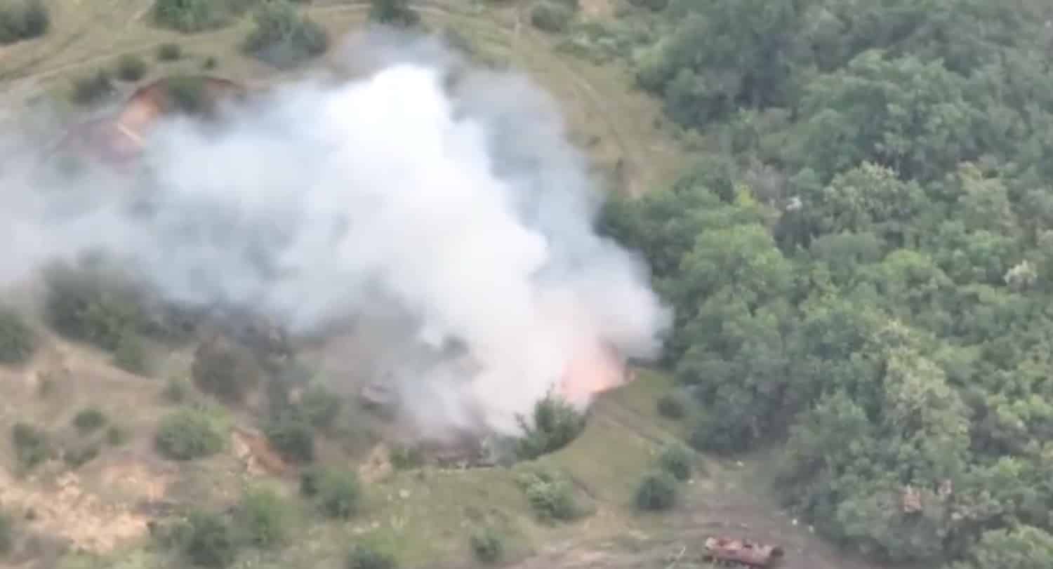 Aerial video frame of thick white smoke rising from a wooded gully.