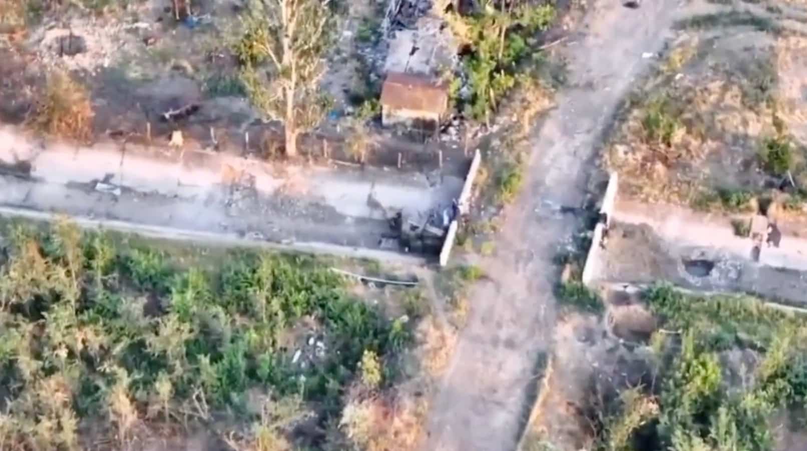 Aerial footage of a road and treeline where troops are sheltering near a bridge.