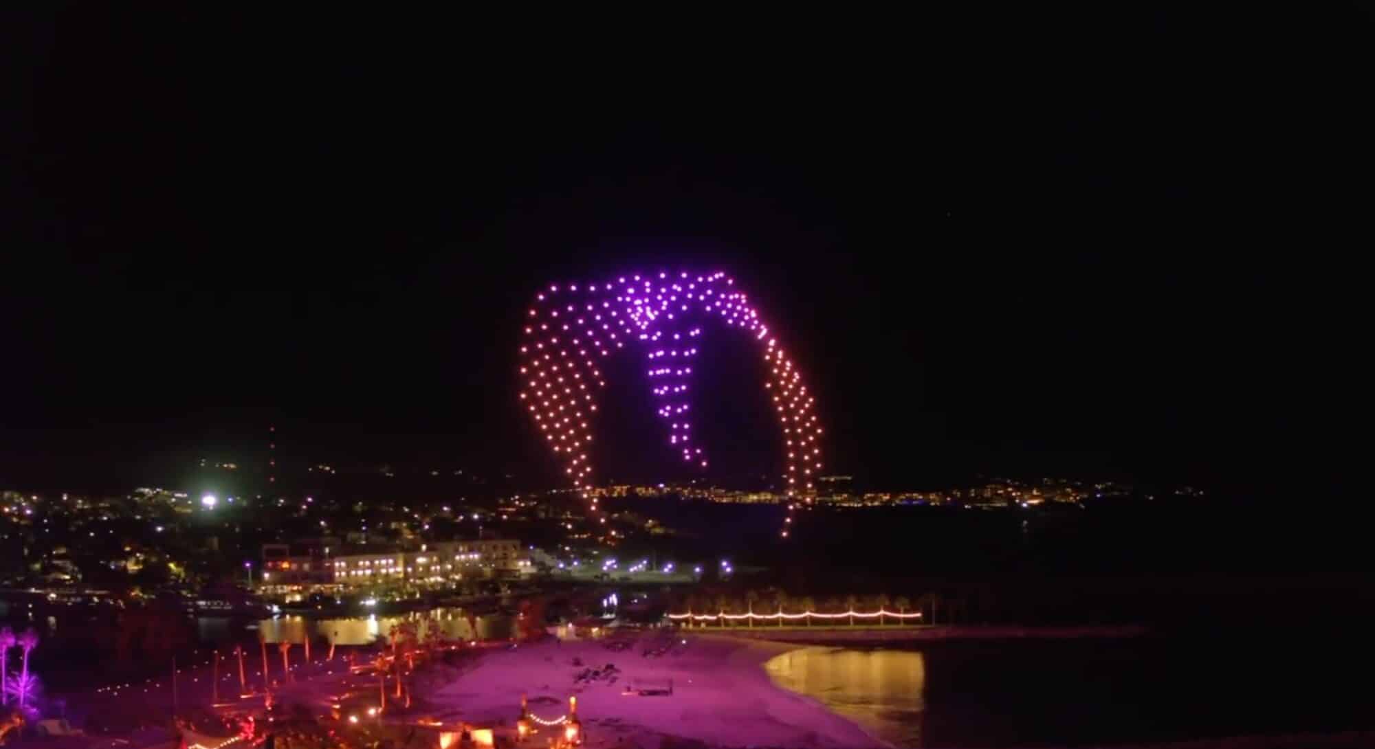 Drone light show glowing pink above a harbor city at night.