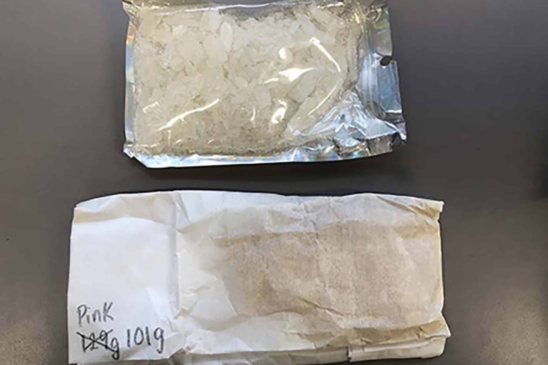 Clear bag of crystal methamphetamine beside a labeled paper evidence package.
