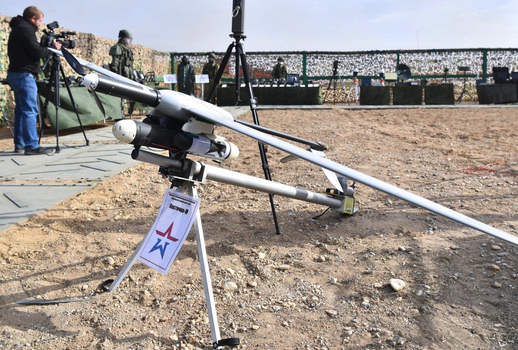 Lastochka-M drone displayed on a tripod stand outdoors as photographers look on.