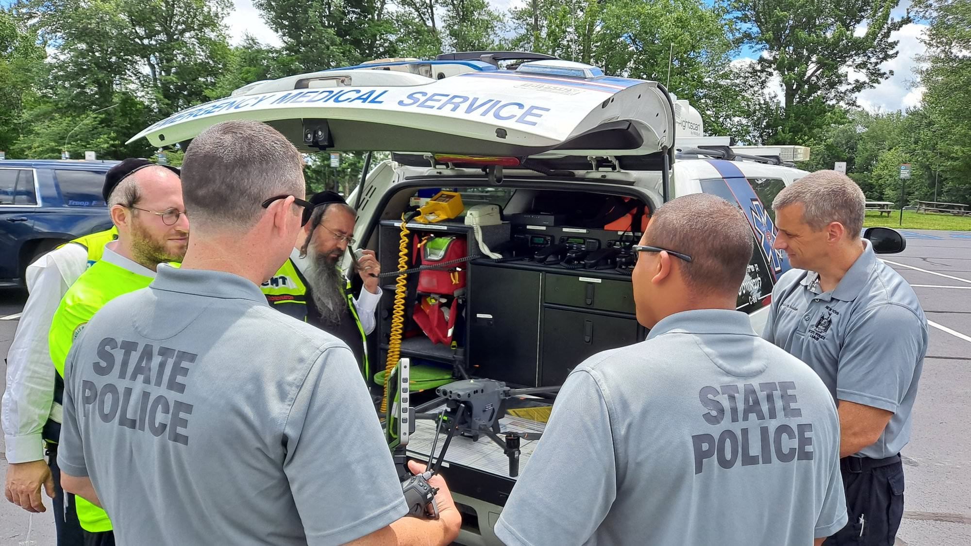 State Police and ambulance crew members inspecting a drone at a rescue vehicle.