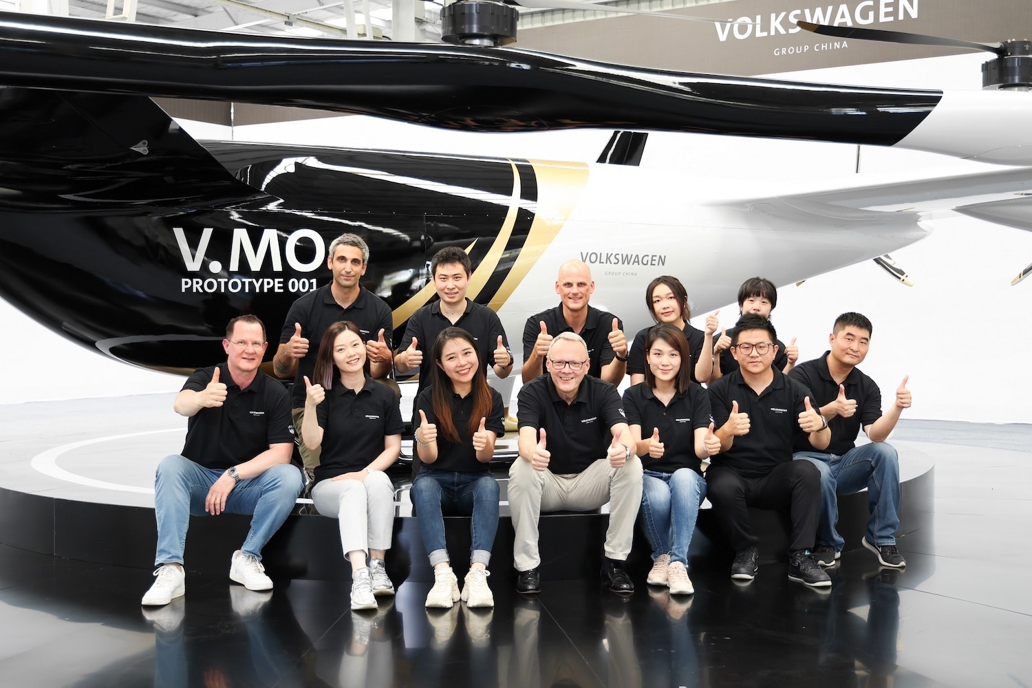 Volkswagen Group China team poses with thumbs up beneath the V.MO prototype.