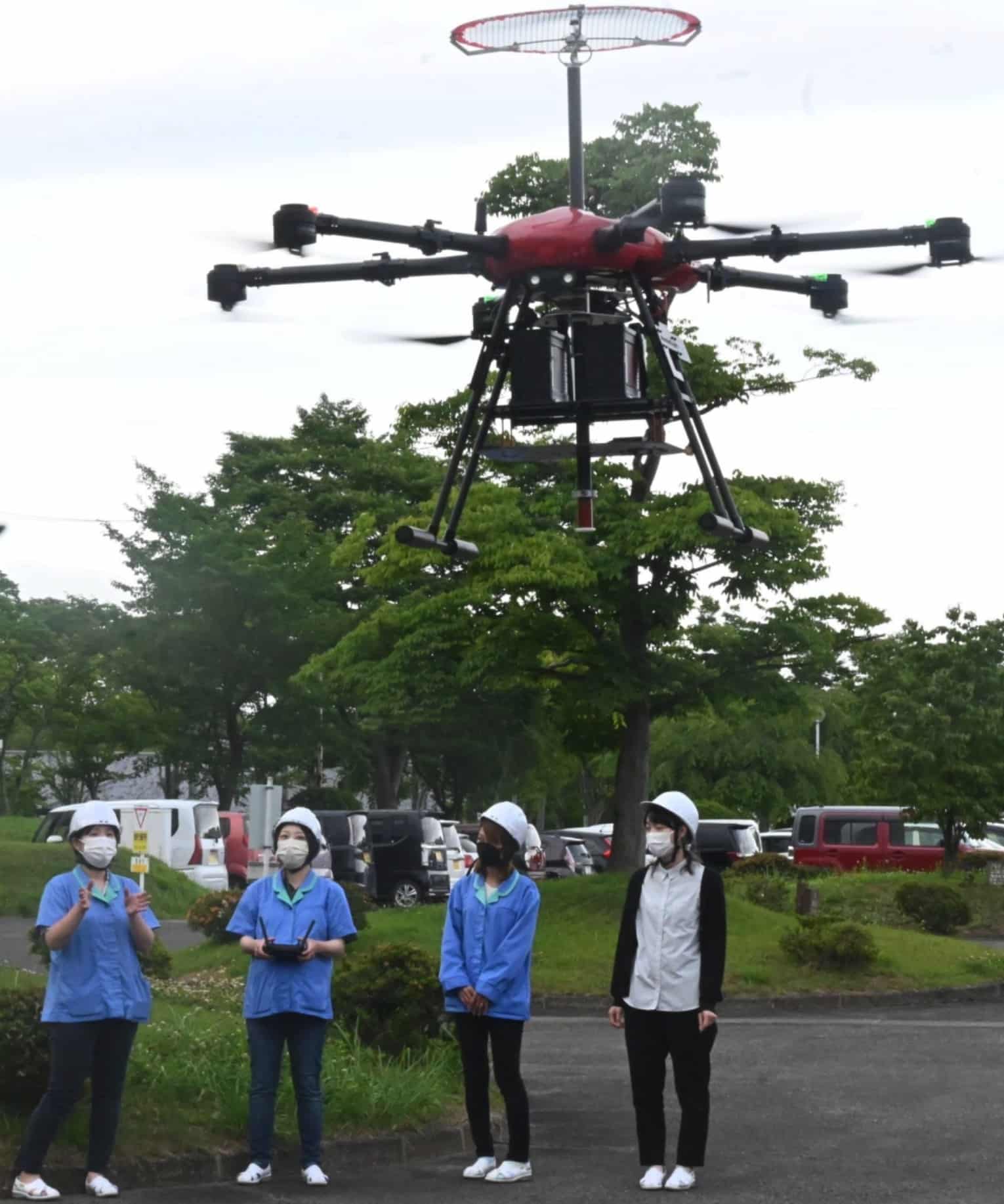 Inspection drone carrying a circular mesh contact ring as technicians watch from below.