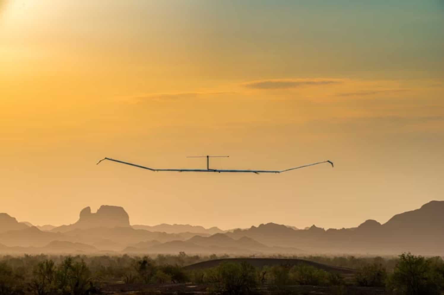 Airbus Zephyr solar aircraft with a long slender wing flying over desert at dawn.