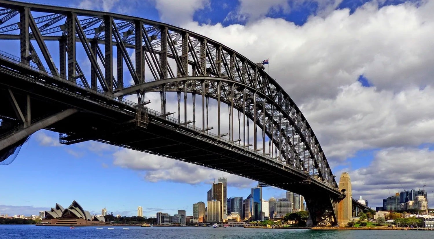 Sydney Harbour Bridge steel arch seen from below with the Opera House beyond.