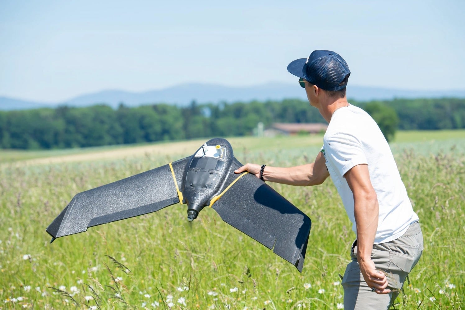 Operator hand-launching a senseFly eBee fixed-wing mapping drone across a summer meadow.