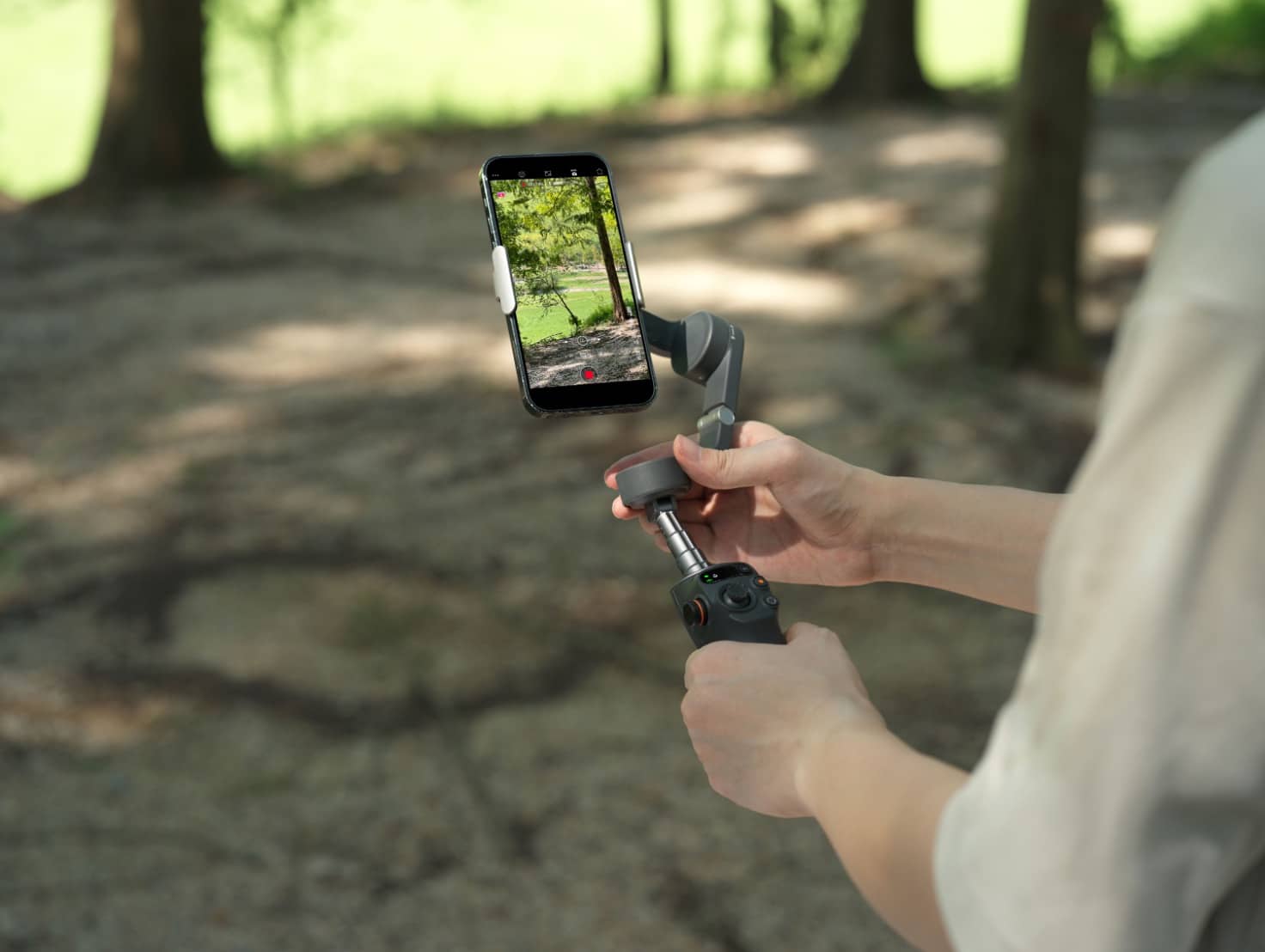 Filming with the Osmo Mobile 6 handheld gimbal on a shaded forest trail.