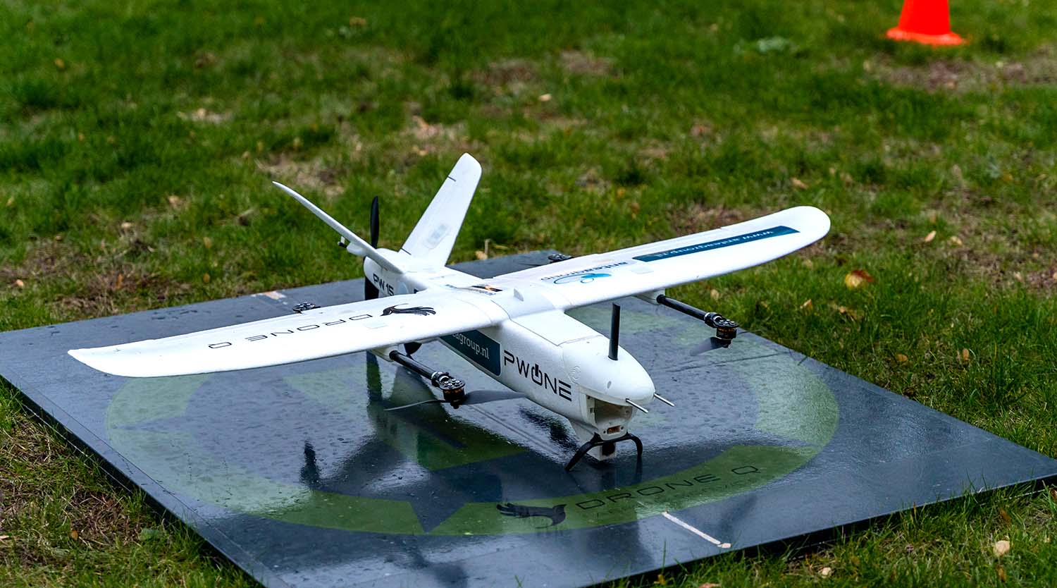 PW One fixed-wing VTOL drone standing on a launch mat in a grassy field.