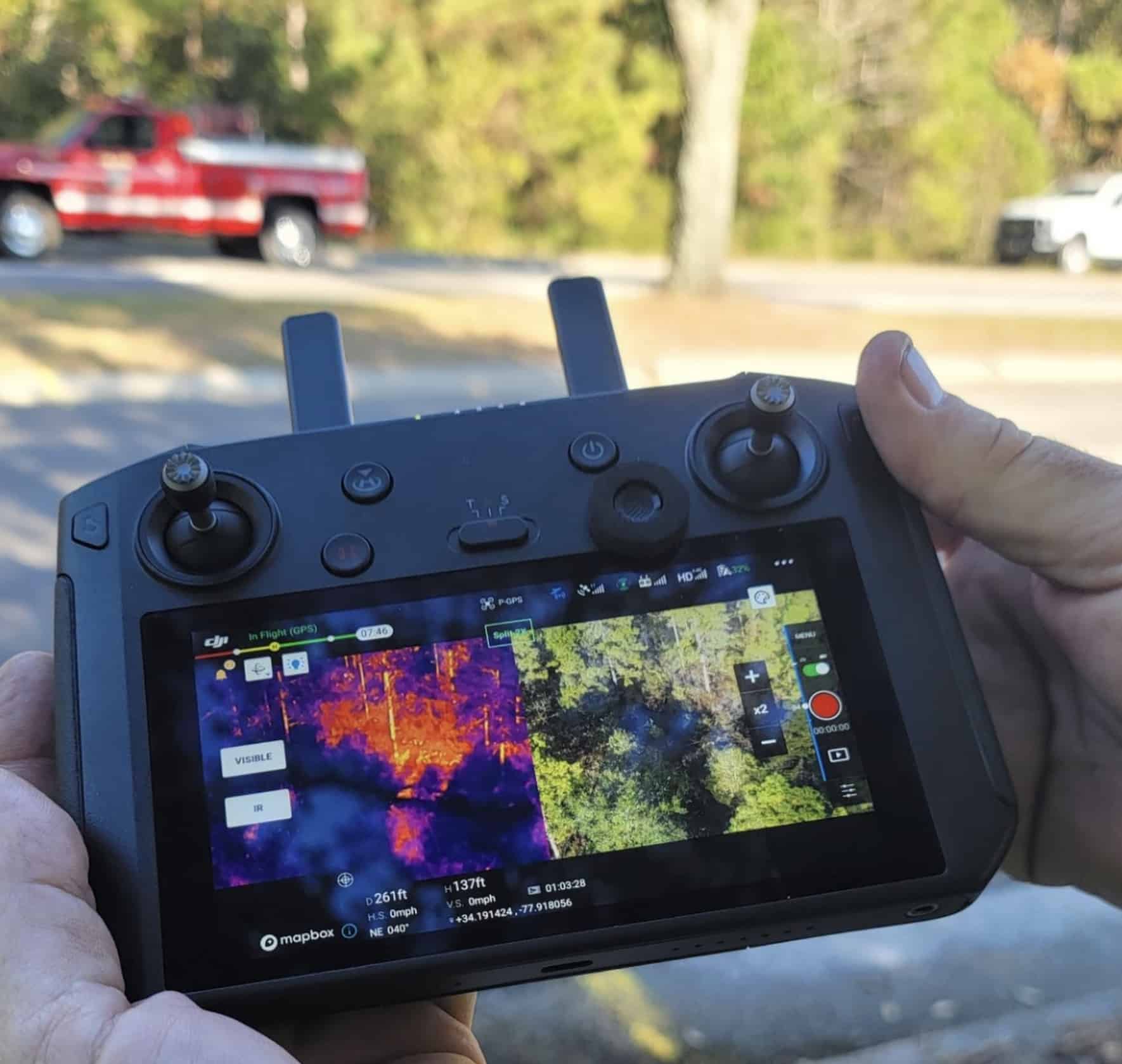 Hands hold a smart controller showing split thermal and visible views of woodland.