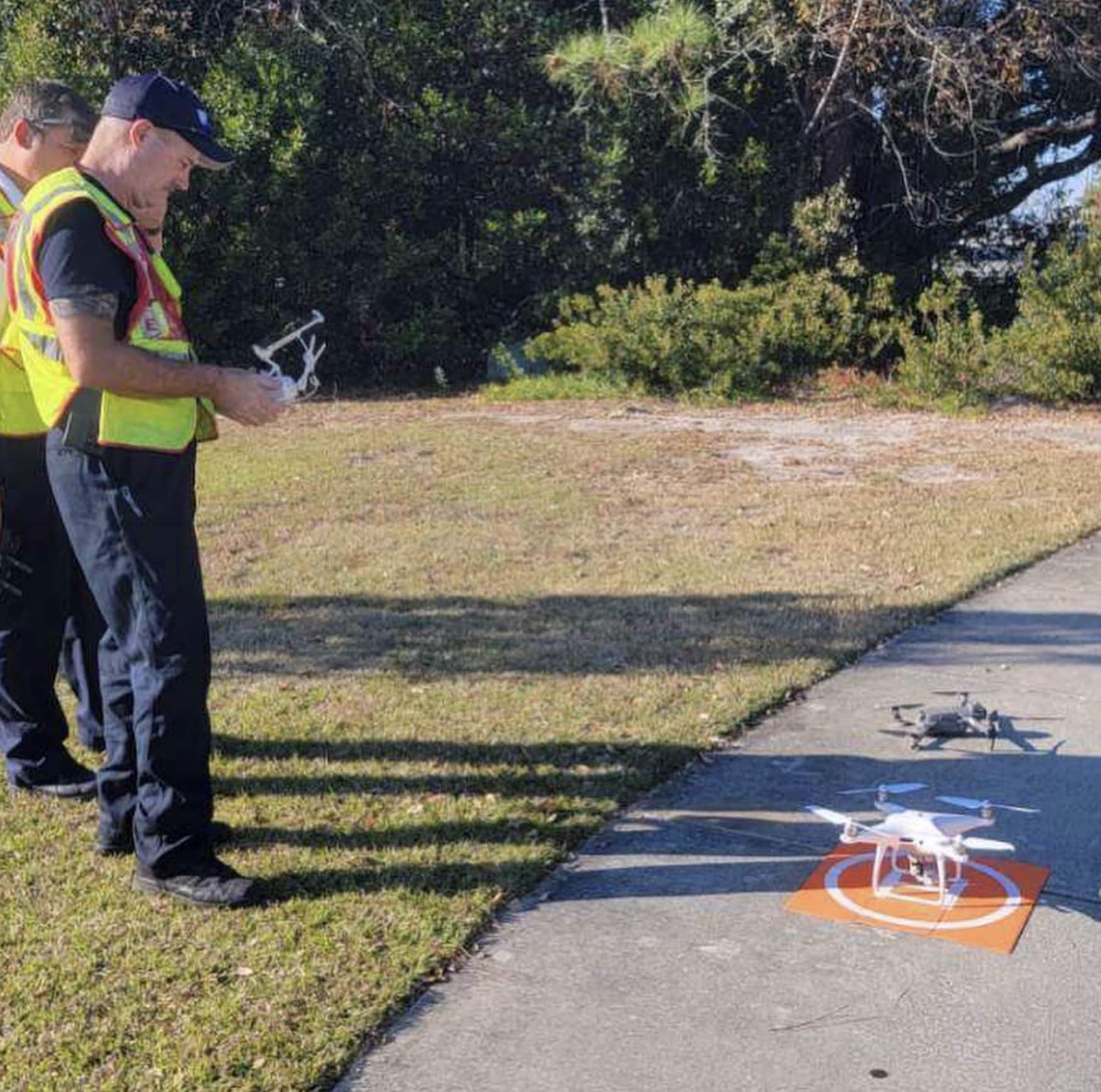 Firefighters in hi-vis vests launch a Phantom drone from an orange landing pad.