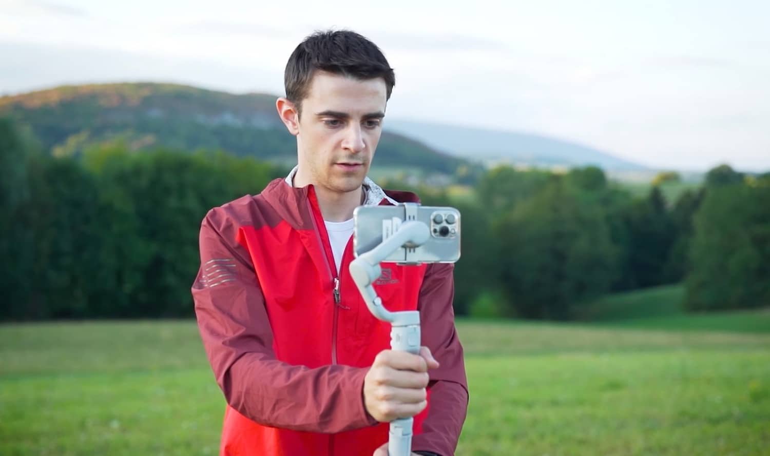 Crew member filming a trail runner with a smartphone on the DJI Osmo Mobile 5.