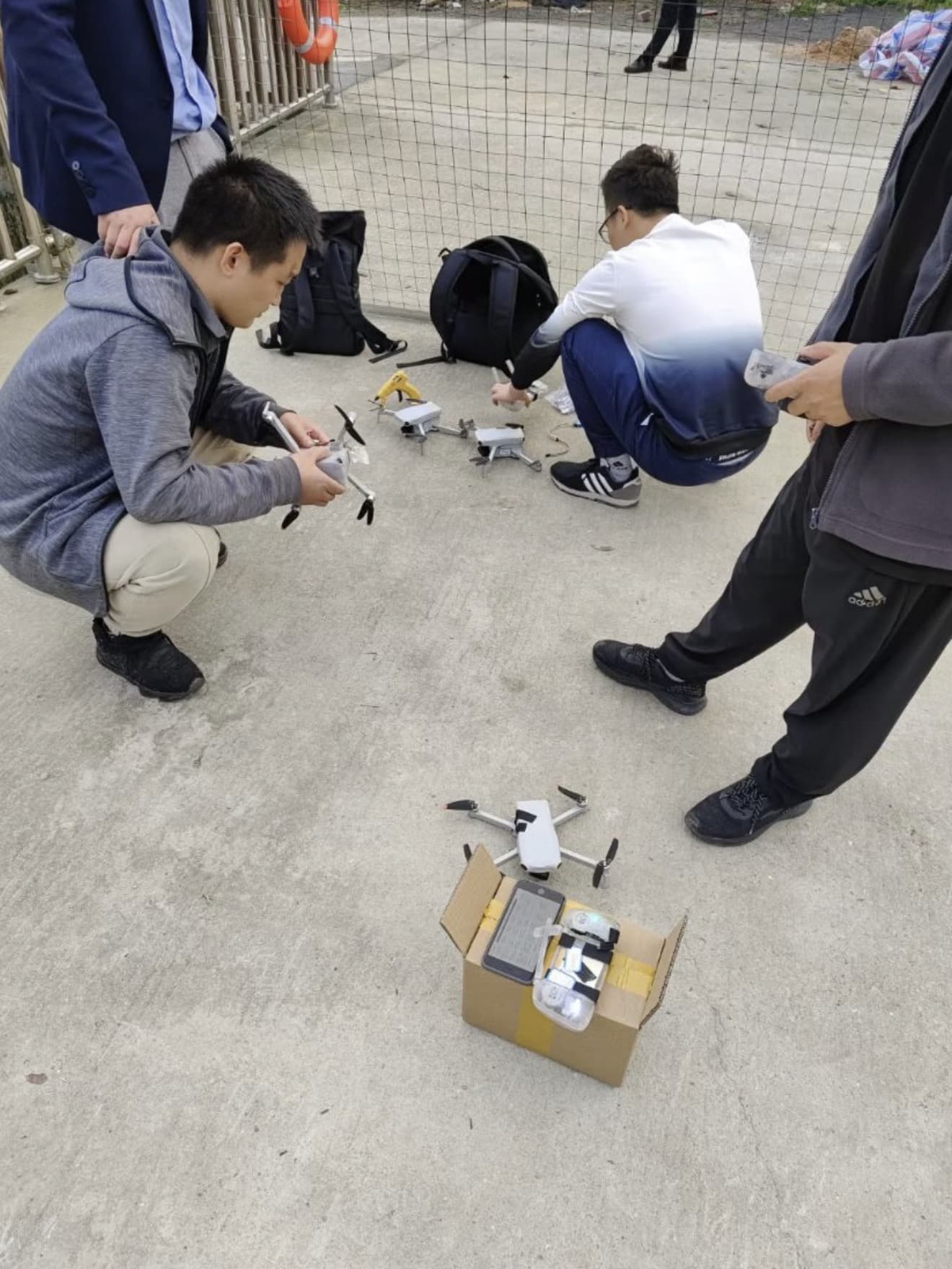 Leaked photo of people crouched around two grey mini drones and their boxes.
