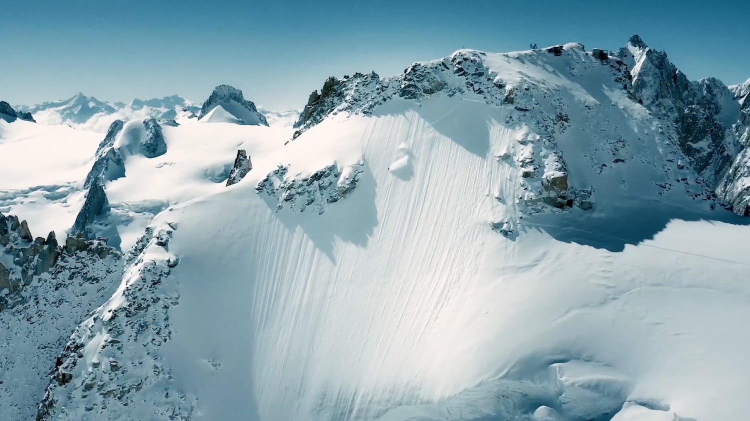 Aerial view of a sunlit snow-covered mountain ridge and its glacier.