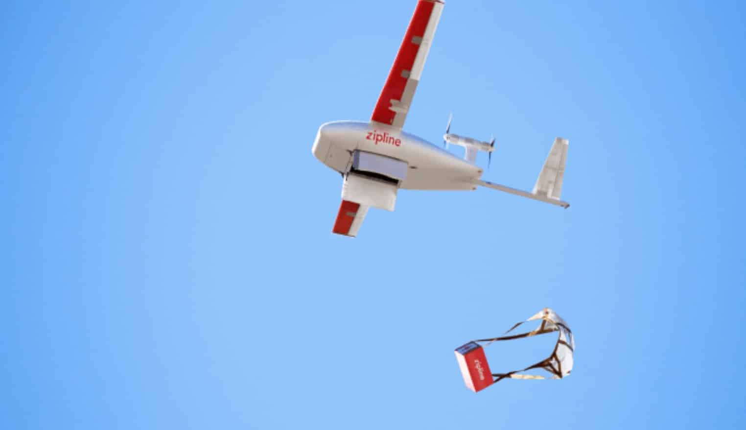 Zipline fixed-wing aircraft releasing a parachute-borne package against a blue sky.