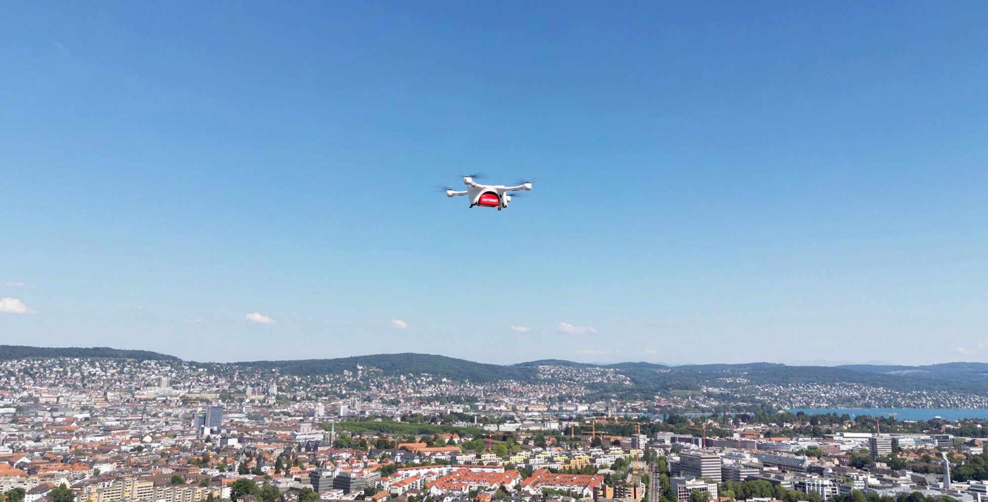 Matternet delivery drone flying high above the Zurich skyline and lake.