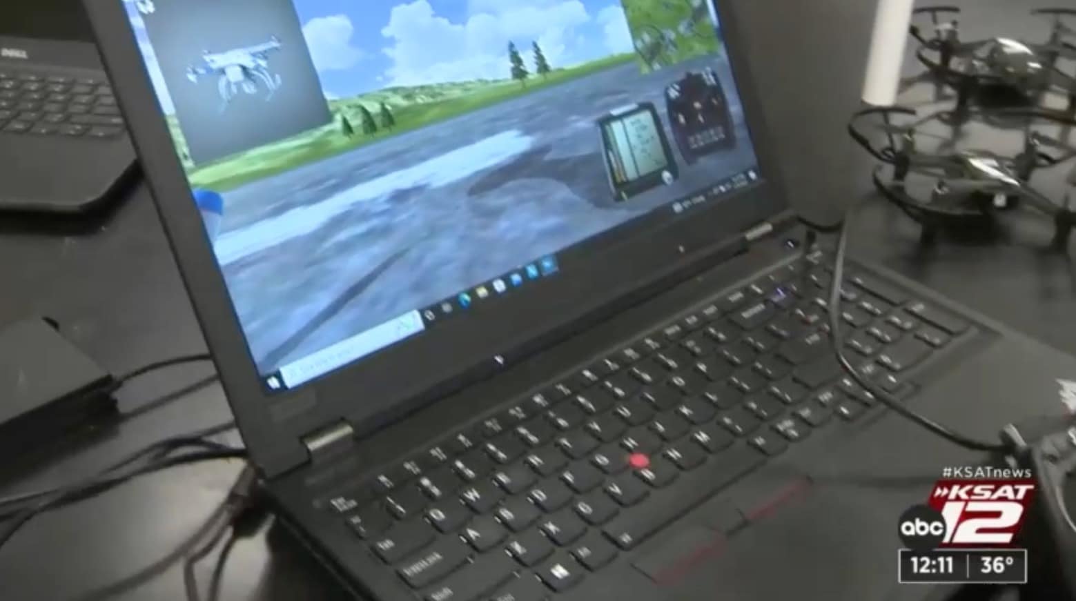 Laptop running a drone flight simulator next to a small training quadcopter.
