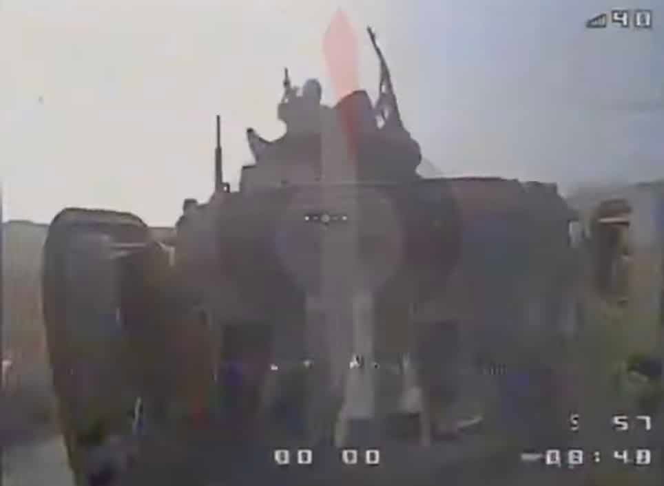 FPV drone camera view descending on a moving Russian BMP with soldiers riding on top.