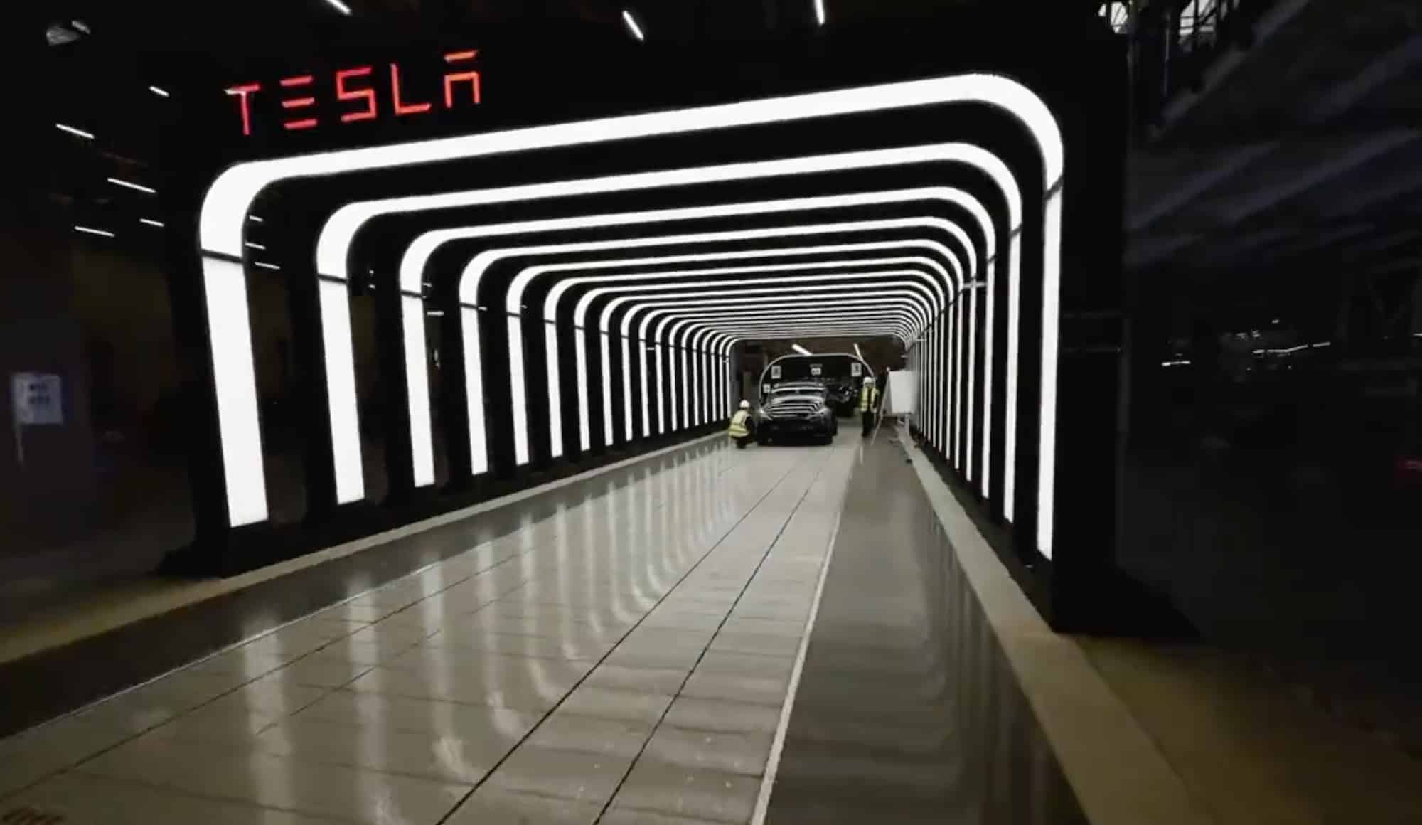 FPV view flying down an illuminated tunnel toward a Tesla sign at Giga Berlin.